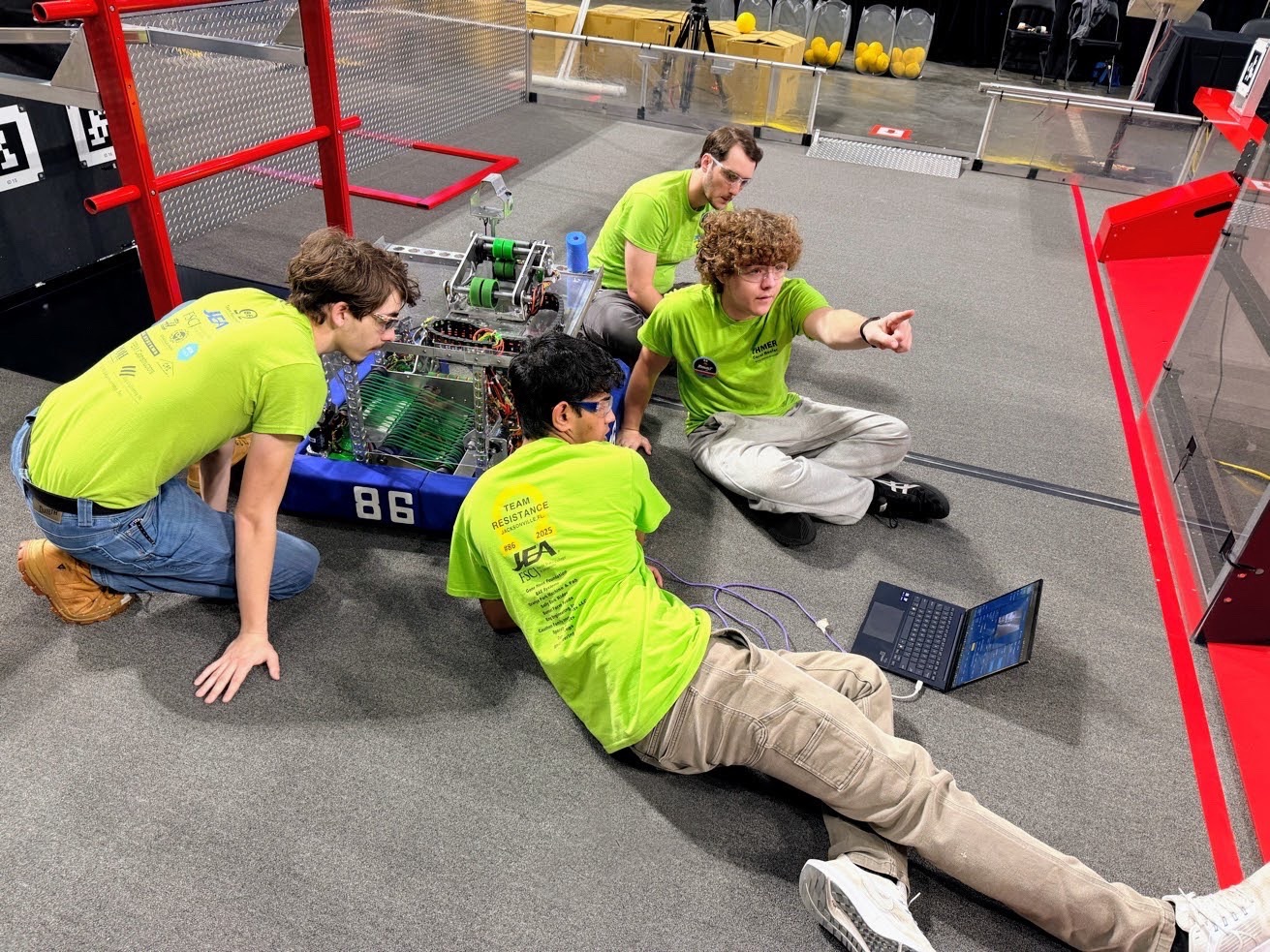 Four students crouched around the robot on the competition field with a laptop tethered to it