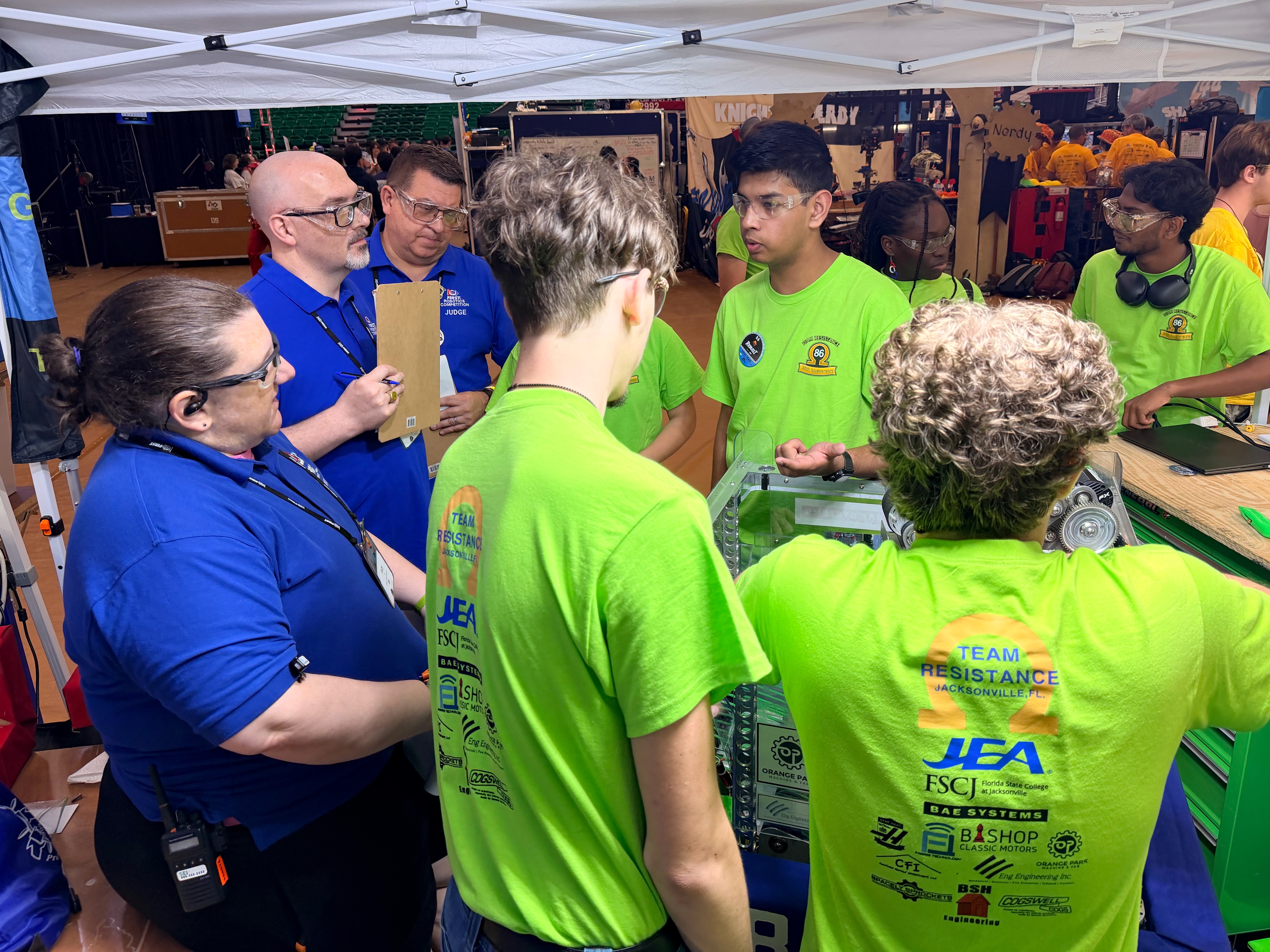 Students in green team shirts presenting their robot to FIRST judges under the pit canopy