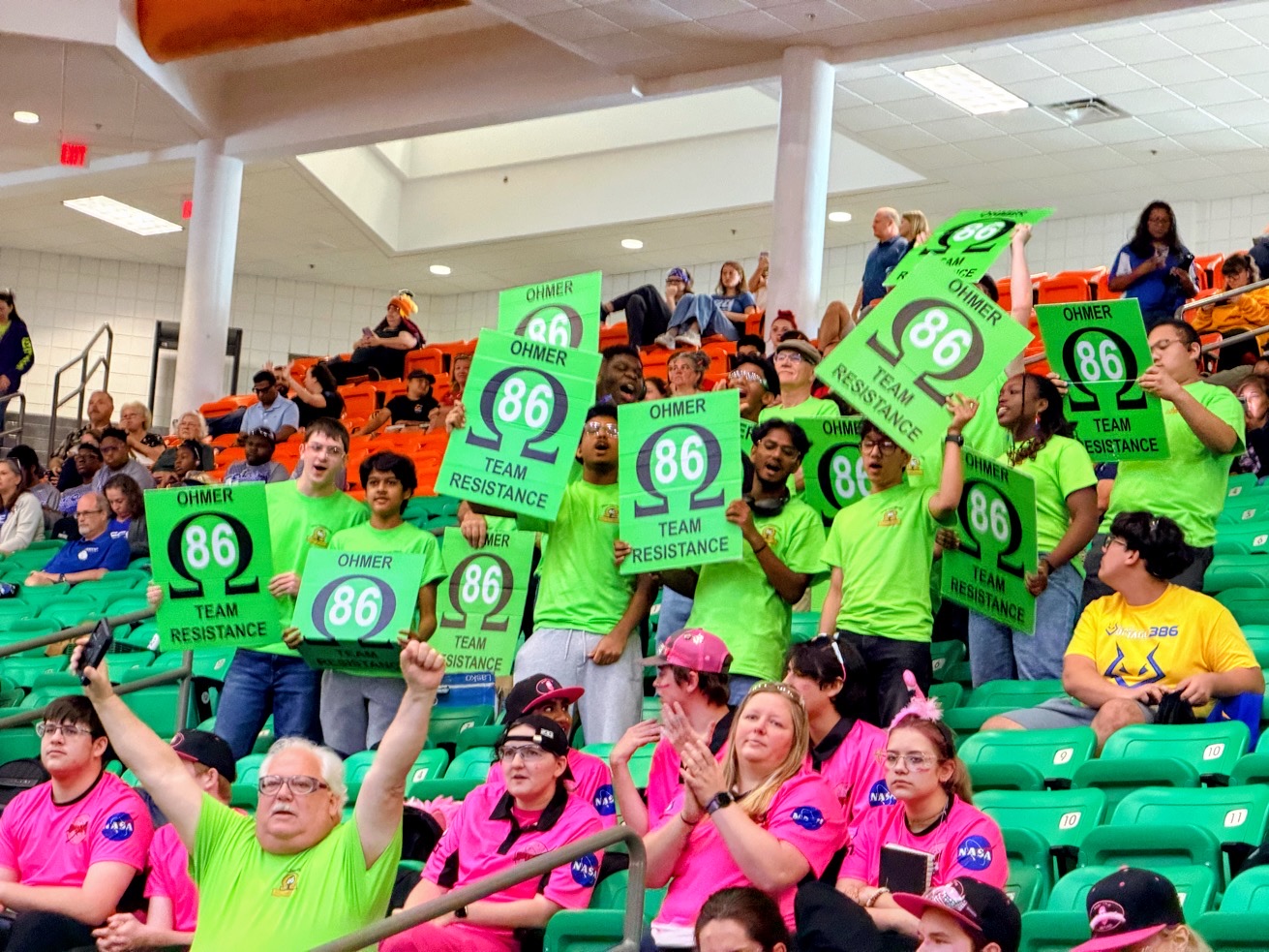 Supporters in arena seating raising green OHMER 86 signs above their heads